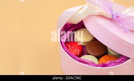 Quattro Macaron francesi dai colori vivaci in scatola di cartone rosa su sfondo di pesca. Foto Stock