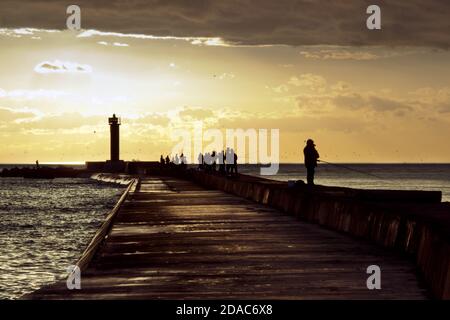 Vista del tramonto con silhouette di gente che pesca al Mar Baltico Sul molo di Mangalsala a riga Foto Stock
