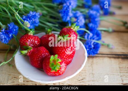 Fiori estivi di stagione (fiori di mais blu) e frutta (cocomero e fragole) su tavolo rustico in legno scottato Foto Stock