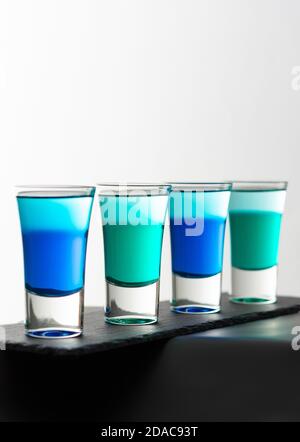 Foto alcoliche blu e verde, bicchieri da shot con liquore colorato su una tavola nera primo piano Foto Stock