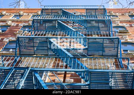 Vista ad angolo basso delle scale blu di fuga del fuoco montate all'esterno della parete dell'edificio in mattoni, utilizzate per l'uscita di emergenza Foto Stock