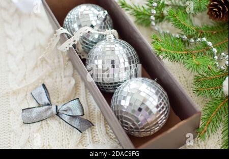 Scatola con tre sfere a specchio, arco d'argento, gerlands, nastri per la decorazione dell'albero di Natale e ramo di abete su sfondo bianco lavorato a maglia Foto Stock