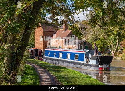 una chiatta di canale o una barca stretta che passa sotto alcuni alberi sul canale di grand union a braunston, northamptonshire, uk Foto Stock