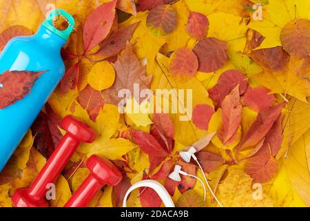 Ciao settembre. Sfondo autunno con manubri, bottiglia d'acqua, cuffie, braccialetto fitness e foglie. Foto Stock