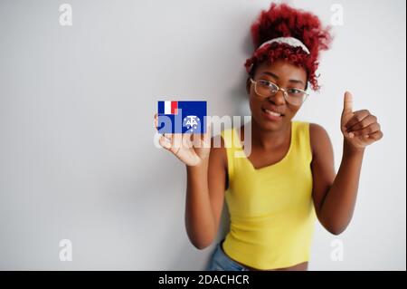 Donna africana con capelli afro, indossare singlet giallo e occhiali, tenere francese Southern Territories bandiera isolato su sfondo bianco, mostrare pollice in su. Foto Stock