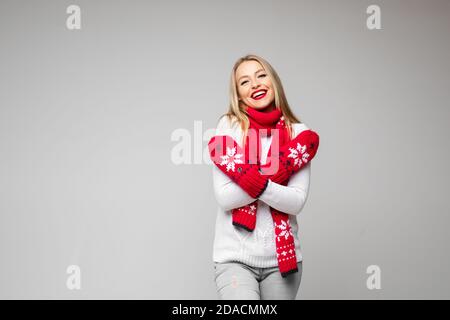 donna attraente in pullover bianco, sciarpa rossa e sorrisi di mitens rossi Foto Stock