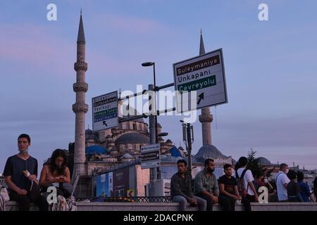 Le persone che siedono sul marciapiede di strada guardando il tramonto con la Nuova Regina Madre Moschea sullo sfondo, Istanbul, Turchia Foto Stock