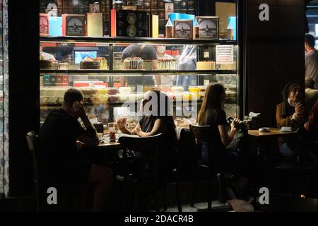 Gente locale con maschere viso rilassante e con bevande e dessert fuori una pasticceria in serata, Istanbul, Turchia Foto Stock