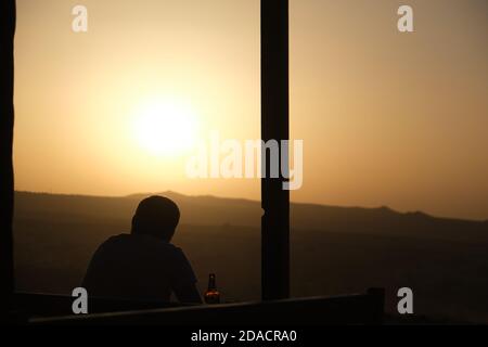 Silhouette sul retro di un uomo rilassante e guardando il tramonto con una bottiglia di birra al Red Valley Panorama Lookout, Cappadocia, Turchia Foto Stock