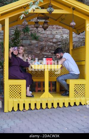 Fidanzate turche scattano una foto selfie in una cabina di mangiare giallo luminoso dell'Antik Cafe nella zona alla moda di Balat, Istanbul, Turchia Foto Stock