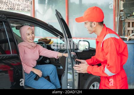 Il meccanico in uniforme rossa apre la porta dell'auto quando il cliente viene alla vettura per essere riparato in l'officina di riparazione Foto Stock