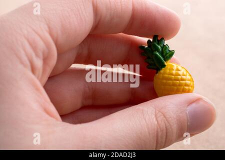 Mano che tiene un piccolo ananas miniatura su uno sfondo sul display Foto Stock