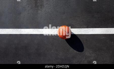 la palla da basket a righe arancioni si erge sulla linea bianca segnando il campo da gioco con asfalto asfalto, oggetto sportivo illuminato dalla luce solare sul parco giochi Foto Stock