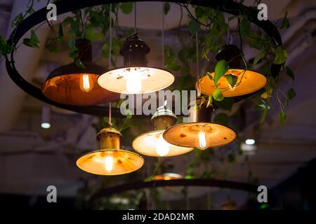 diverse lanterne rotonde pendenti in stile retrò loft con lampade edison brillano con luce calda all'interno del ristorante scuro, closeup di lampade appese, nobo Foto Stock