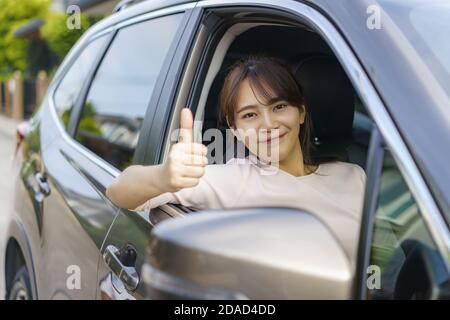 Asian felice giovane bella donna che guida una macchina e pollice in su nel sedile anteriore con sorriso prepararsi a viaggiare con la sua auto. Foto Stock