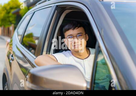 Asian felice giovane bell'uomo che guida un'auto sul sedile anteriore con un sorriso preparati a viaggiare con la sua auto. Foto Stock