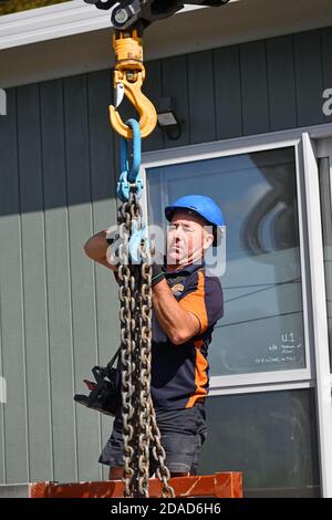 GREYMOUTH, NUOVA ZELANDA, 21 OTTOBRE 2020: Un operatore di gru lavora per sollevare un piccolo edificio da un camion sui suoi pali. Foto Stock