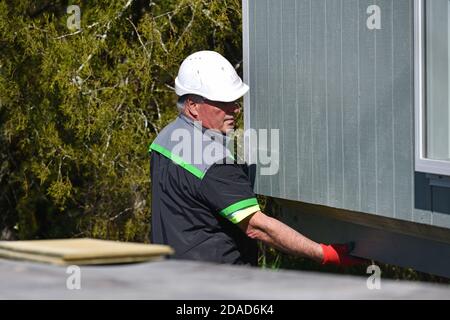 GREYMOUTH, NUOVA ZELANDA, 21 OTTOBRE 2020: Un operatore di gru lavora per sollevare un piccolo edificio da un camion sui suoi pali. Foto Stock