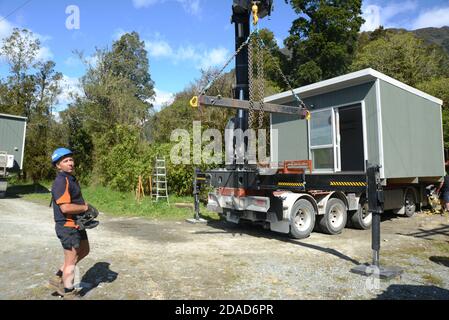 GREYMOUTH, NUOVA ZELANDA, 21 OTTOBRE 2020: Un operatore di gru lavora per sollevare un piccolo edificio da un camion sui suoi pali. Foto Stock