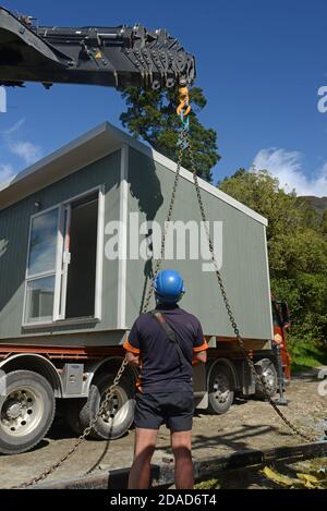 GREYMOUTH, NUOVA ZELANDA, 21 OTTOBRE 2020: Un operatore di gru lavora per sollevare un piccolo edificio da un camion sui suoi pali. Foto Stock