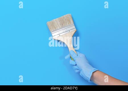 Pennello per vernice in mano su sfondo blu. Pennello con manico in legno di una mano umana con spazio per la copia Foto Stock