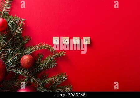 Alberi di Natale con palline rosse e la vendita di parola fatta di lettere di legno su uno sfondo rosso. Vista dall'alto. Vendita stagionale. Foto Stock