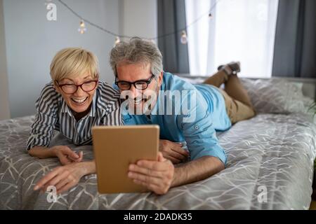 Bella coppia sorridente matura che si diverte mentre si usa tablet a. casa Foto Stock