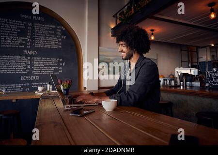 Punta giovane imprenditore maschile digitando sul portatile con auricolare seduto in una caffetteria moderna Foto Stock