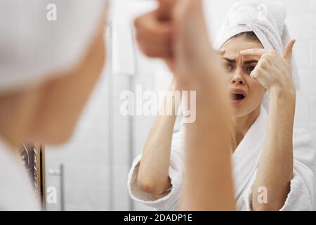 la donna stringe i pimples sul suo viso vicino allo specchio Foto Stock