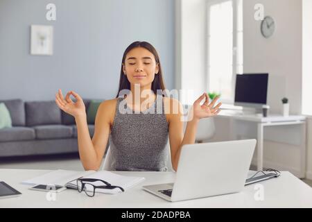 Calma donna di affari medita con i suoi occhi chiusi nel suo ufficio durante una pausa. Foto Stock