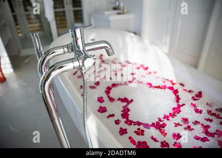 Interno di bagno moderno. Romantico bagno di lusso idea per la coppia. Vasca da bagno in marmo nero con petali di rosa rossa, decorata con candele, bagno Foto Stock