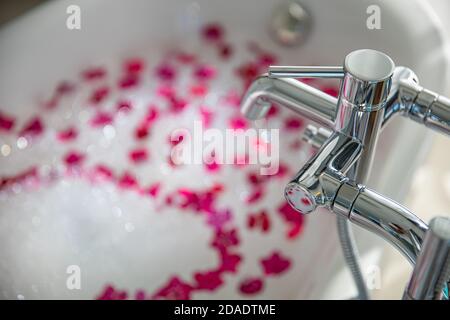 Interno di bagno moderno. Romantico bagno di lusso idea per la coppia. Vasca da bagno in marmo nero con petali di rosa rossa, decorata con candele, bagno Foto Stock