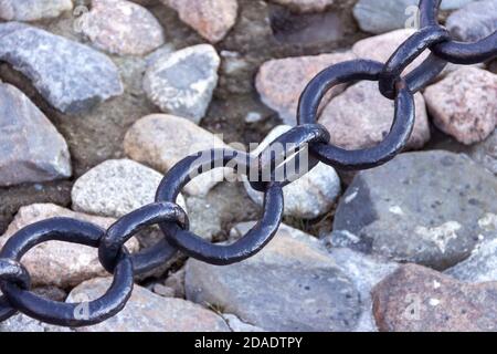 Vecchia catena arrugginita forgiata con vernice che si spellano sullo sfondo delle pietre di pavimentazione. Foto Stock