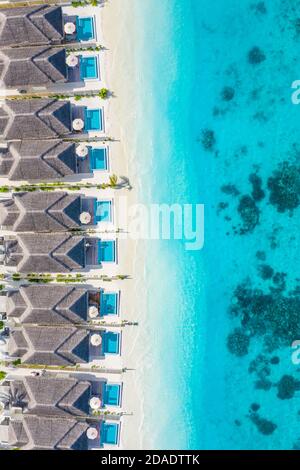 Atolli e isole nelle Maldive. Isola tropicale alle Maldive con ville d'acqua di lusso, bungalow su mare blu incredibile. Vacanza estiva, vista aerea Foto Stock