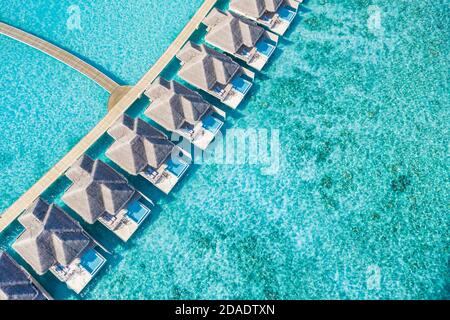 Atolli e isole nelle Maldive. Isola tropicale alle Maldive con ville d'acqua di lusso, bungalow su mare blu incredibile. Vacanza estiva, vista aerea Foto Stock