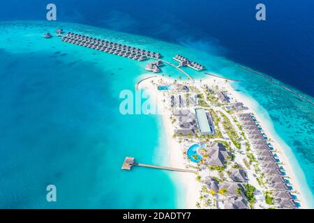 Atolli e isole nelle Maldive. Isola tropicale alle Maldive con ville d'acqua di lusso, bungalow su mare blu incredibile. Vacanza estiva, vista aerea Foto Stock