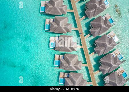 Atolli e isole nelle Maldive. Isola tropicale alle Maldive con ville d'acqua di lusso, bungalow su mare blu incredibile. Vacanza estiva, vista aerea Foto Stock