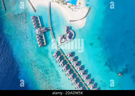 Atolli e isole nelle Maldive. Isola tropicale alle Maldive con ville d'acqua di lusso, bungalow su mare blu incredibile. Vacanza estiva, vista aerea Foto Stock