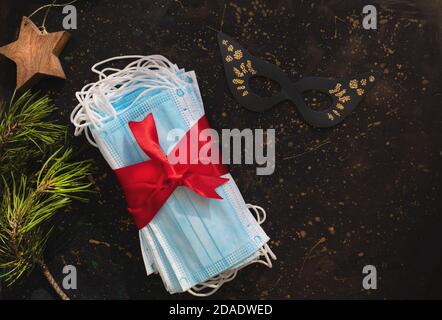 Maschere igieniche come regalo con un nastro rosso incorniciato con rami di abete. Natale e Capodanno 2021 decorazione su uno sfondo scuro. Autoisolamento Foto Stock