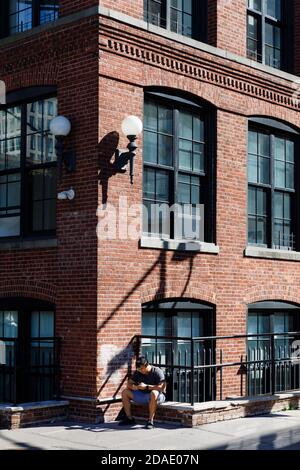 NEW YORK, USA - 22 settembre 2017: Scena di strada a Dumbo, Brooklyn. Un giovane con un telefono cellulare si siede sul parapetto di una casa in mattoni Foto Stock
