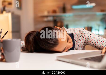Donna addormentata con la testa sul tavolo mentre lavora da casa su una scadenza. Dipendente che utilizza la tecnologia moderna a mezzanotte facendo straordinari per lavoro, affari, carriera, rete, stile di vita, wireless. Foto Stock