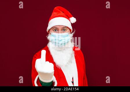 Babbo Natale che mostra il dito medio, indossa una maschera medica.Red studio muro. Foto Stock