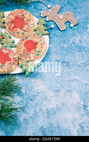 Su sfondo blu, un piatto con biscotti natalizi fatti a mano, rami di pino e una decorazione natalizia a forma di cervo . Orientamento verticale Foto Stock