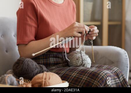 Primo piano di donna seduta sul divano e a maglia il caldo abbigliamento in camera a casa Foto Stock