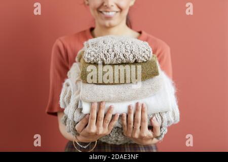 Primo piano di giovane donna che tiene stack o caldo abiti di lana in mano contro lo sfondo rosa Foto Stock