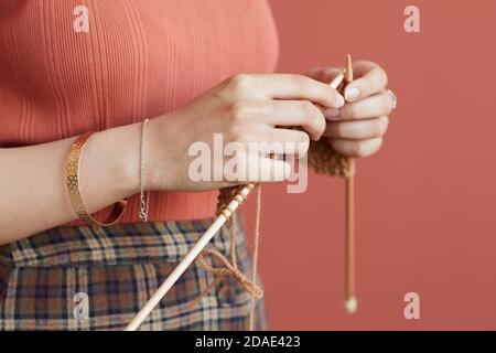 Primo piano di donna che tiene gli aghi di maglieria che si maglia per se stessa in piedi contro lo sfondo rosa Foto Stock