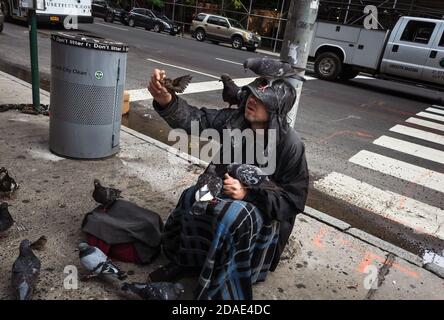 New York, Stati Uniti d'America - 24 settembre 2018: Scena di Manhattan Street. Un uomo senza dimora che alimenta uccelli e piccioni Foto Stock