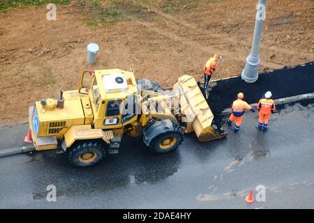 I lavoratori stradali e gli escavatori posano l'asfalto su un terreno umido - Mosca, Russia, 18 maggio 2020 Foto Stock