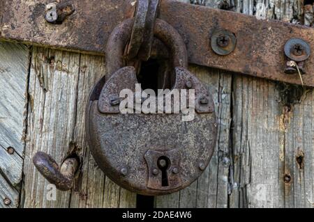 Vecchio blocco antiruggine sulla portiera. Serratura in metallo sul cancello di una vecchia casa colonica. Vero stile villaggio. Dispositivo di chiusura in acciaio antiruggine bloccato con blocco in ferro Foto Stock