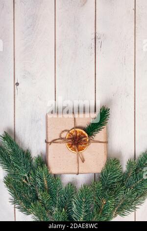 Confezione regalo in stile eco-friendly: Carta naturale ruvida, corda di iuta, ramoscelli di abete rosso su sfondo di legno bianco. Foto Stock